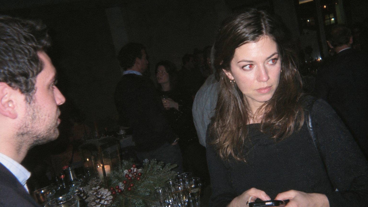 A phone screen records a focused woman at an office holiday party as she prepares to join a conversation