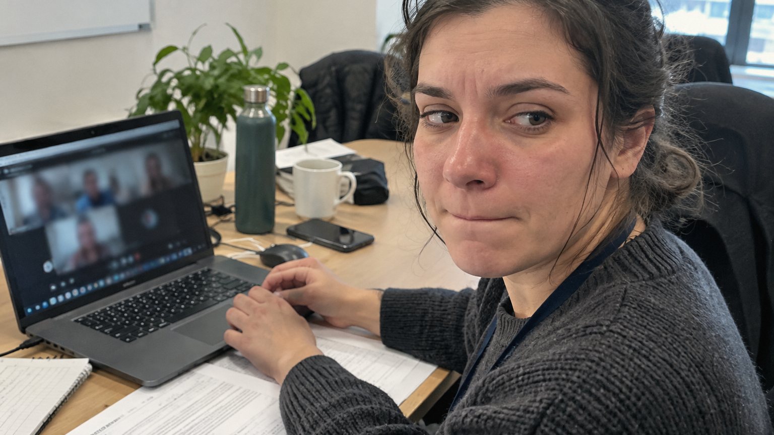 An office worker looks at a laptop after a performance review video call while a review document and pen sit beside the keyboard