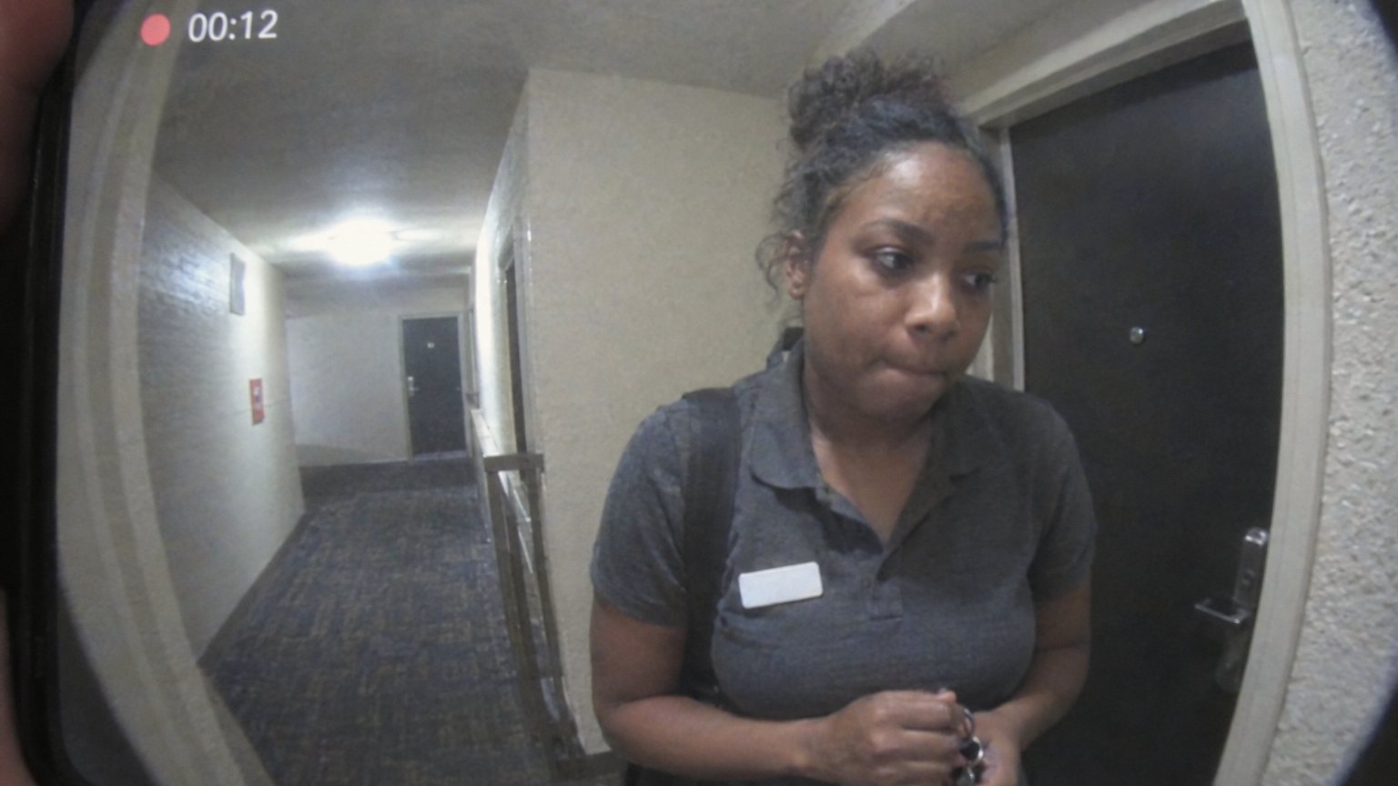 A Black woman in a work polo stands tense at an apartment door after a customer-facing shift